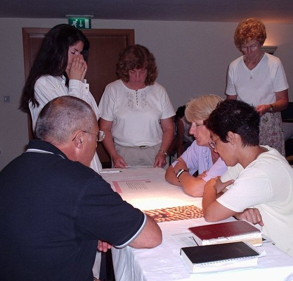 6 people gathered around a table, praying.